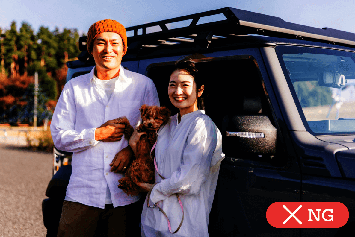 車の前でペットの犬を抱く夫婦の画像